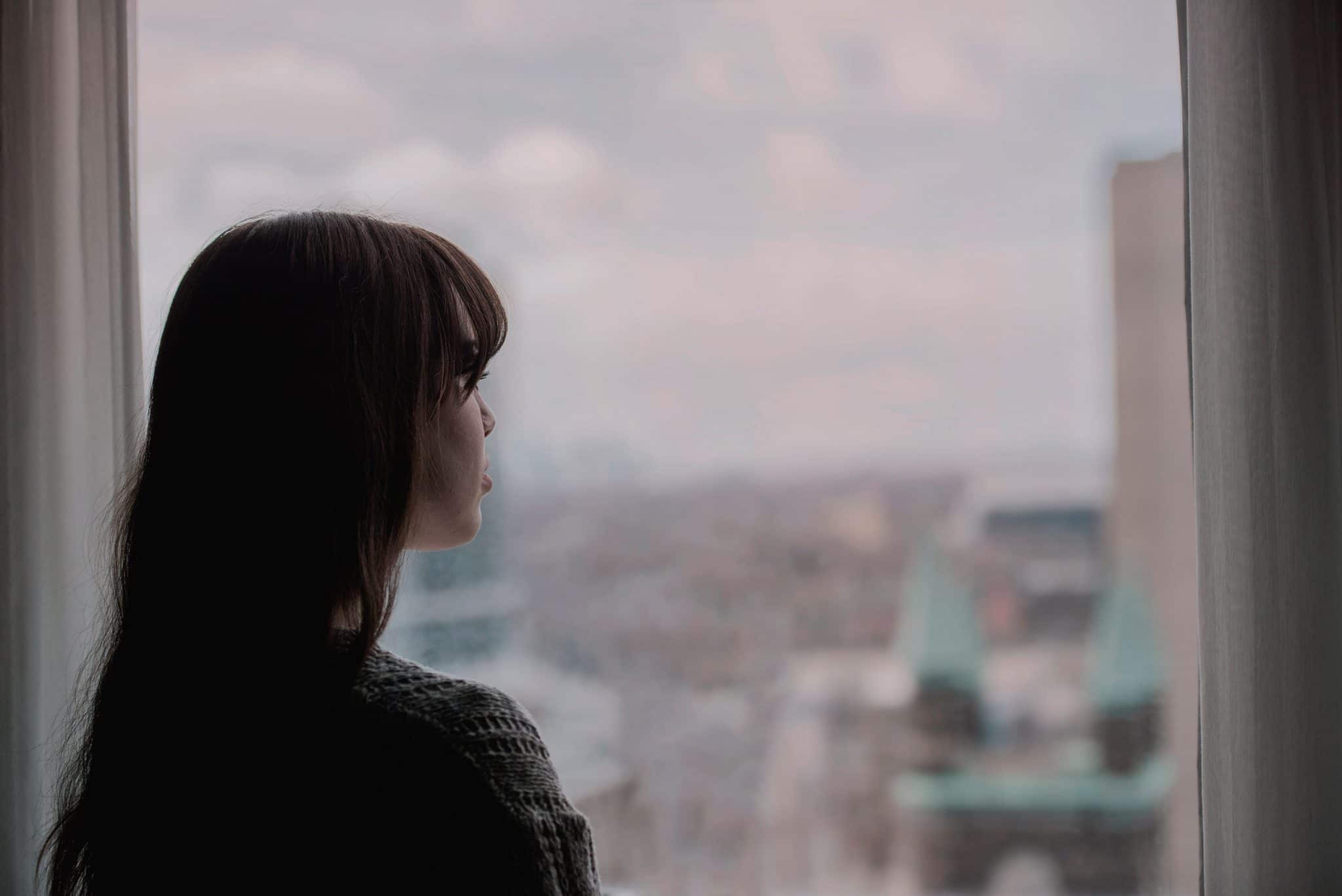 Woman staring out a window at a city.