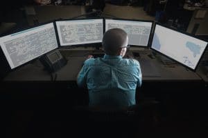 Worker sits a multiple computer screens displaying maps.