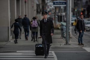 Pilot in uniform crosses the street with luggage.