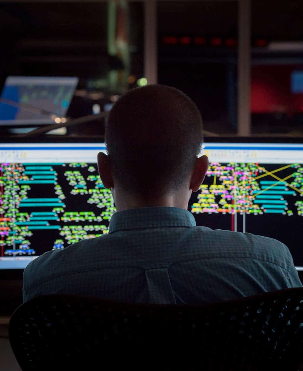 Man sits at two computer screens displaying colourful graphics.