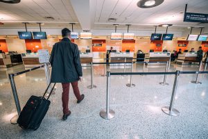 Passenger approaching airport check-in desk with luggage.