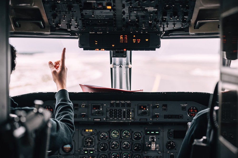 Pilot pointing out cockpit window on runway.
